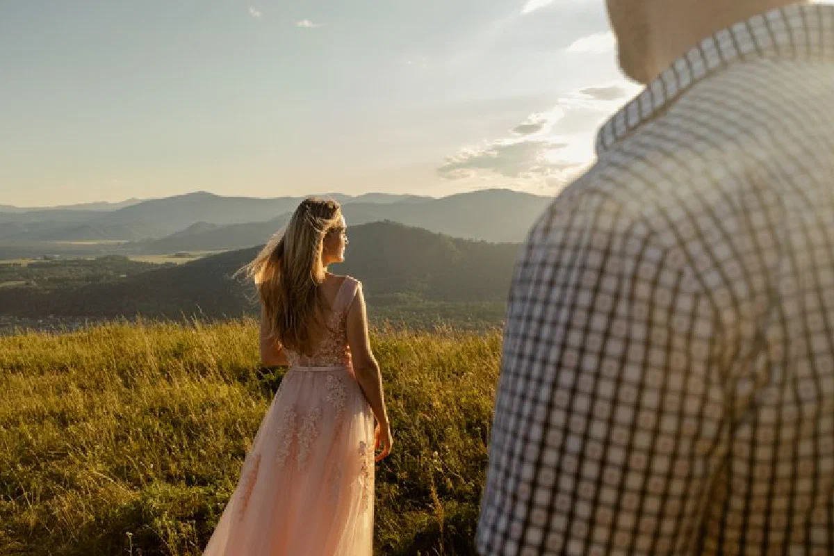 Couple enjoying a serene sunset in a grassy mountain field, capturing romantic ambiance.