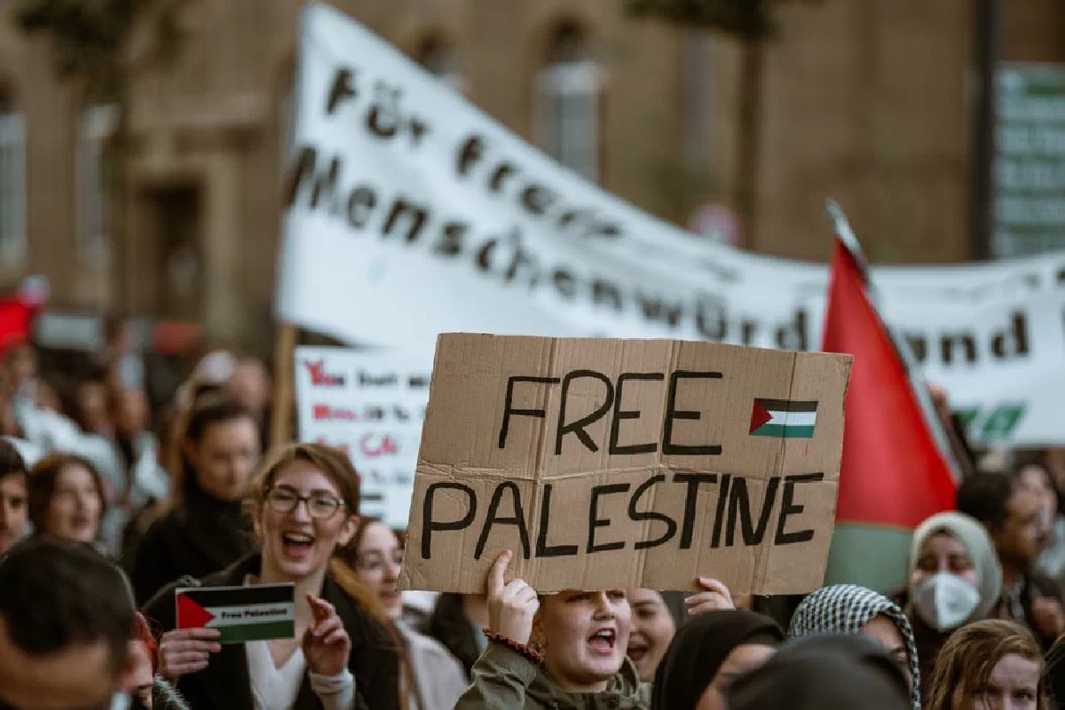A large crowd gathers in a city for a protest holding a Free Palestine sign.