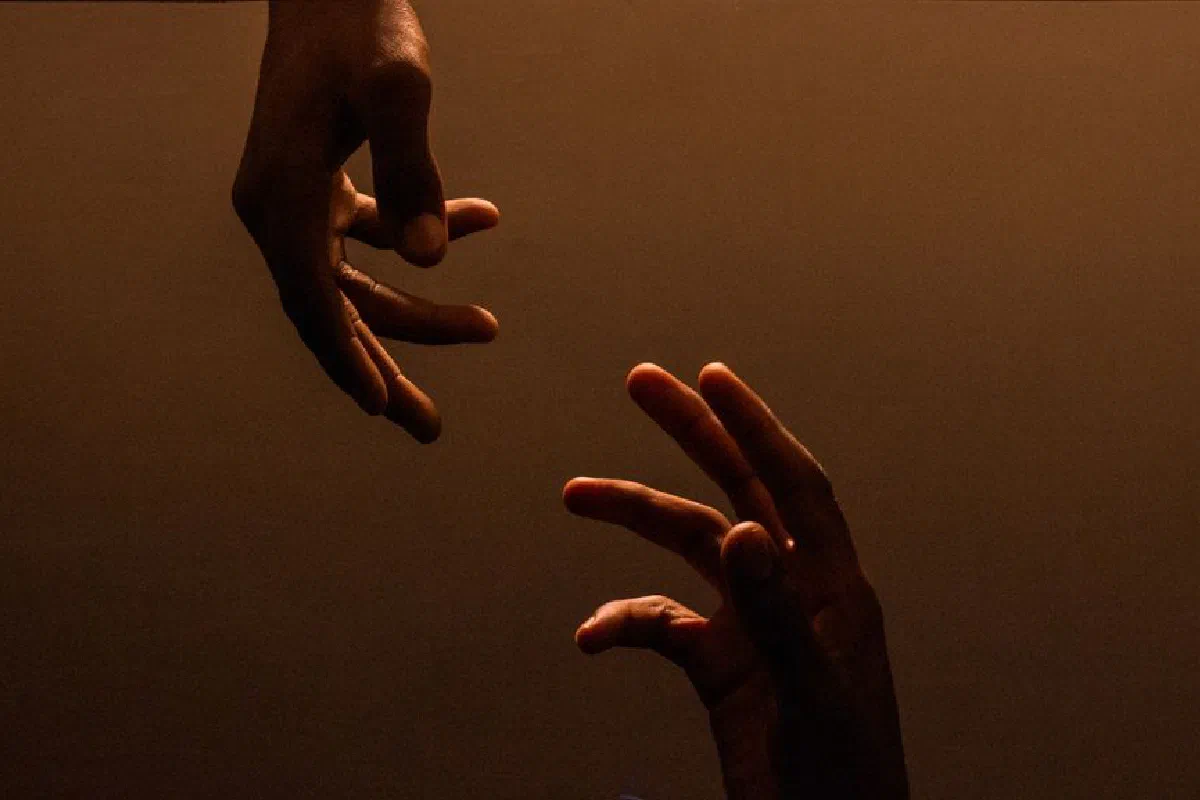 Two hands reaching towards each other against a dark, warm background, symbolizing connection.