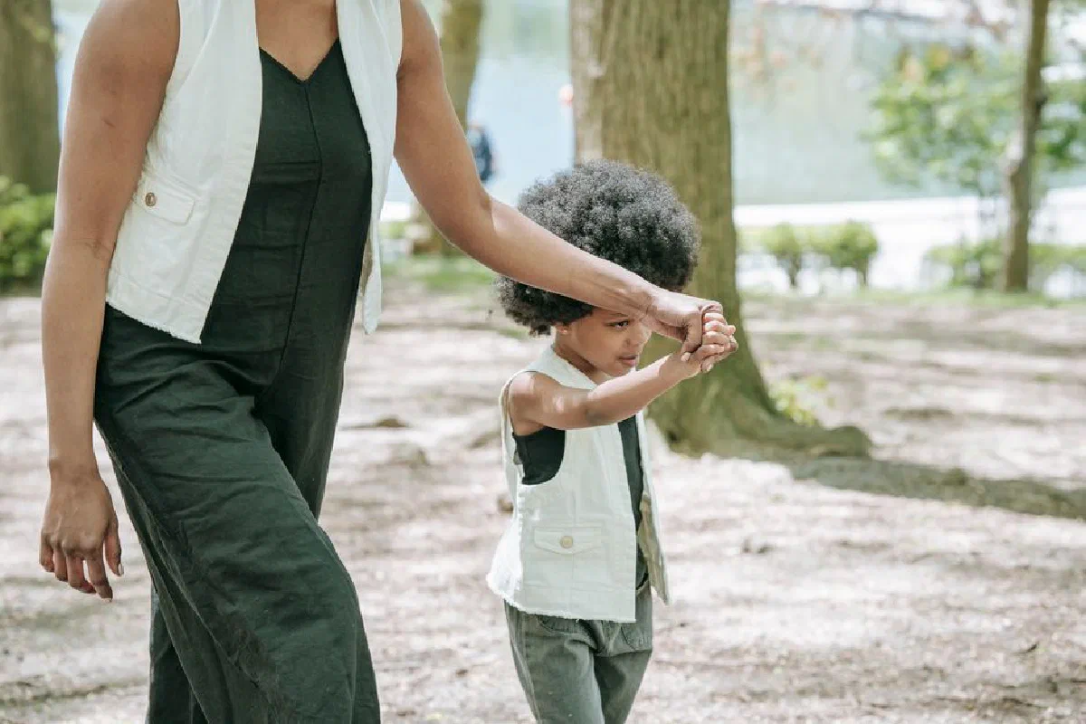 A mother and child holding hands while walking in a park, enjoying a pleasant day outdoors.