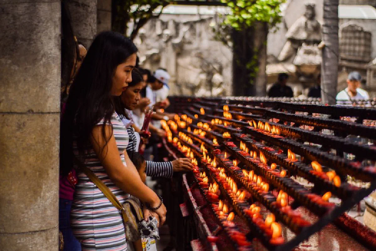 People praying and lighting candles at an outdoor religious altar, with a focus on spirituality and faith.