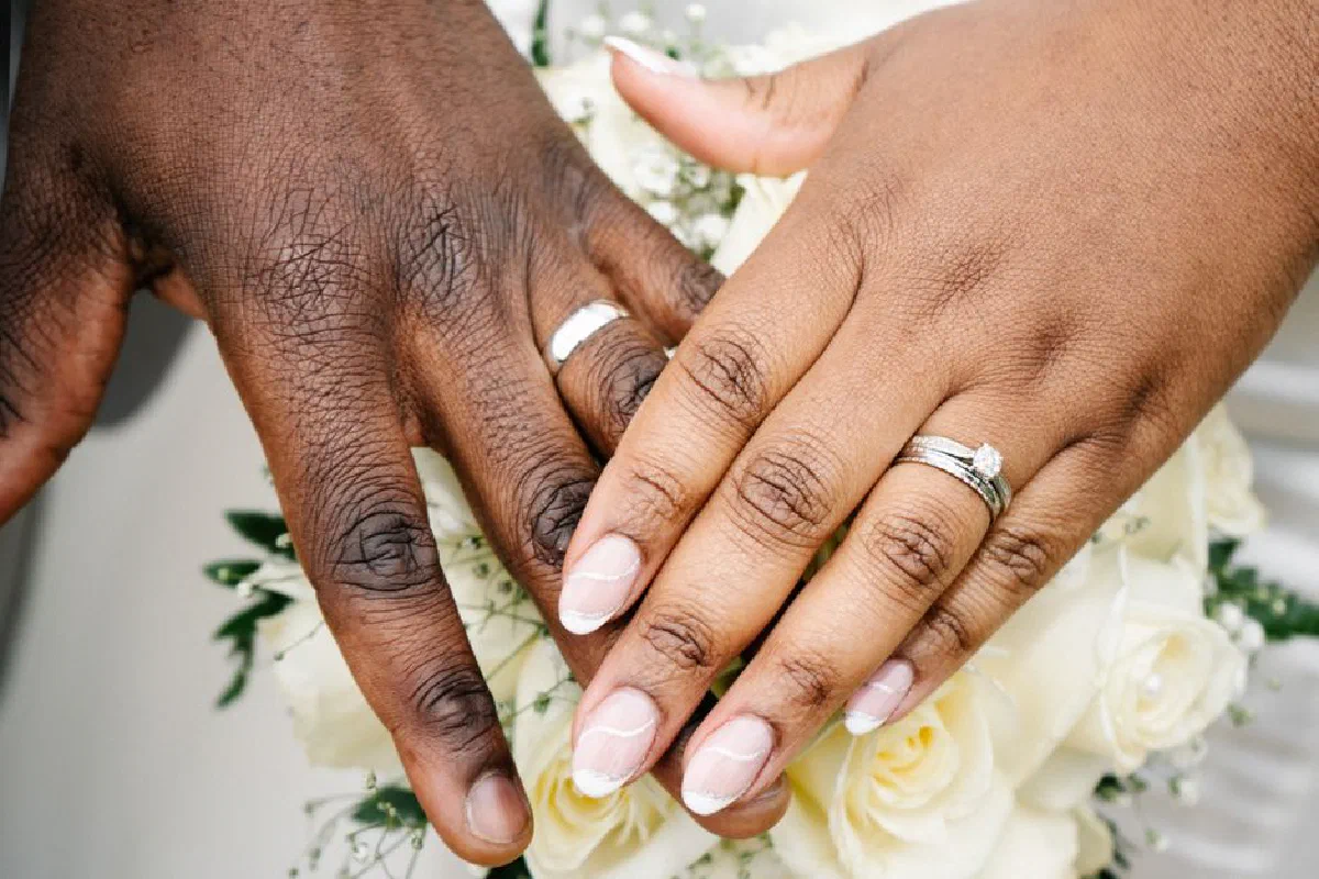Intimate close-up of wedding rings on a couple's hands over a white rose bouquet.