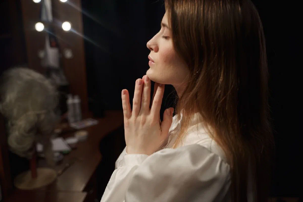 Side view of a woman with hands clasped in prayer, reflecting in a dressing room mirror.