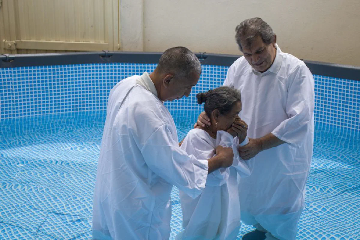 A Christian baptism ceremony with two men and a woman in an indoor pool setting.