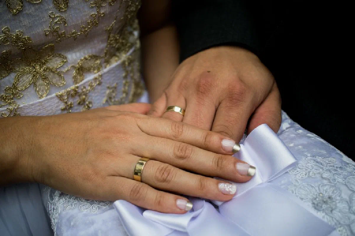 Detailed shot of newlyweds' hands with wedding rings, adorned with intricate lace and embroideries.