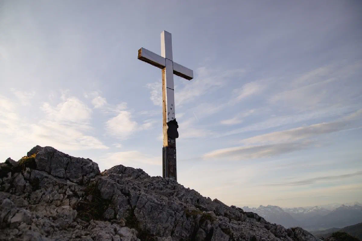 A solitary cross atop a rocky summit in the Bavarian Alps at sunrise.