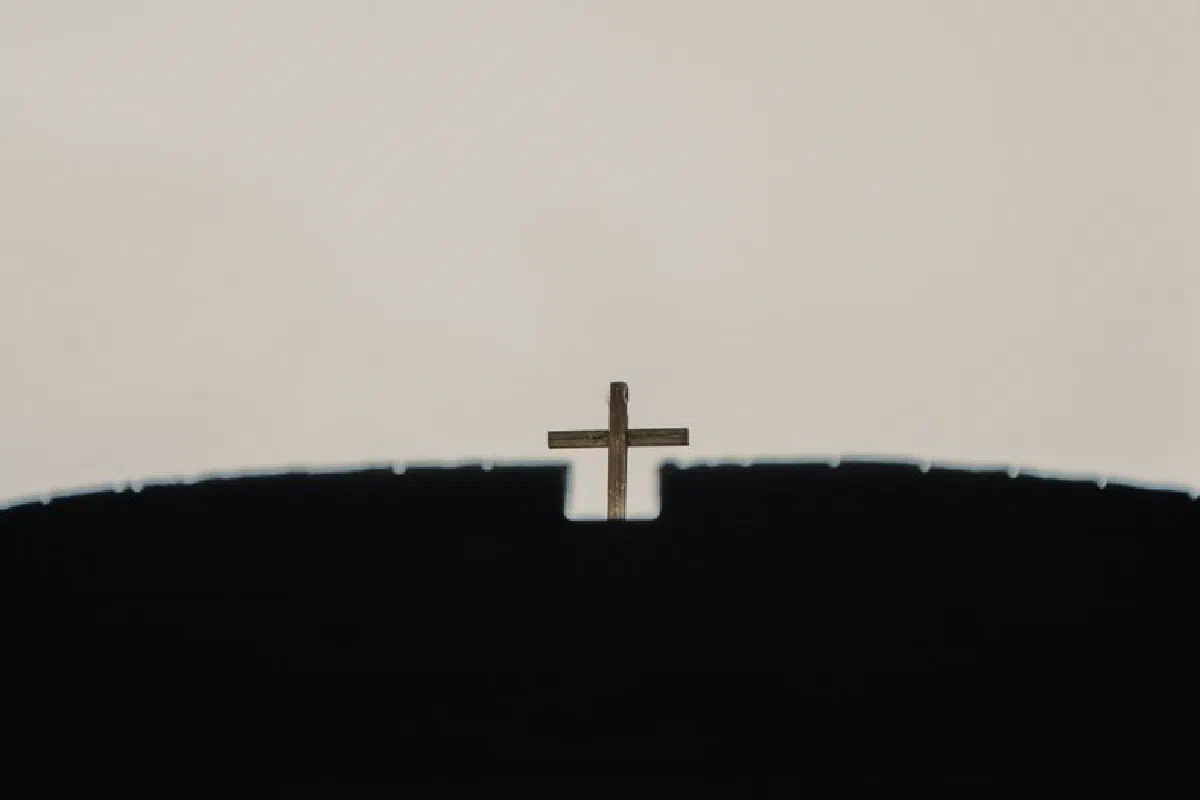 From below of old wooden cross on church roof with ribbed surface under light sky