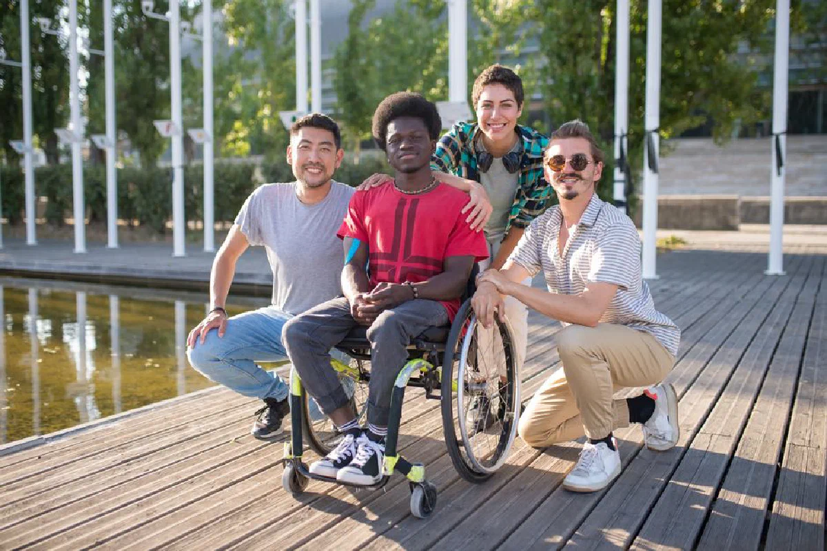 Group of diverse friends, including a person in a wheelchair, enjoying a sunny day at the park.