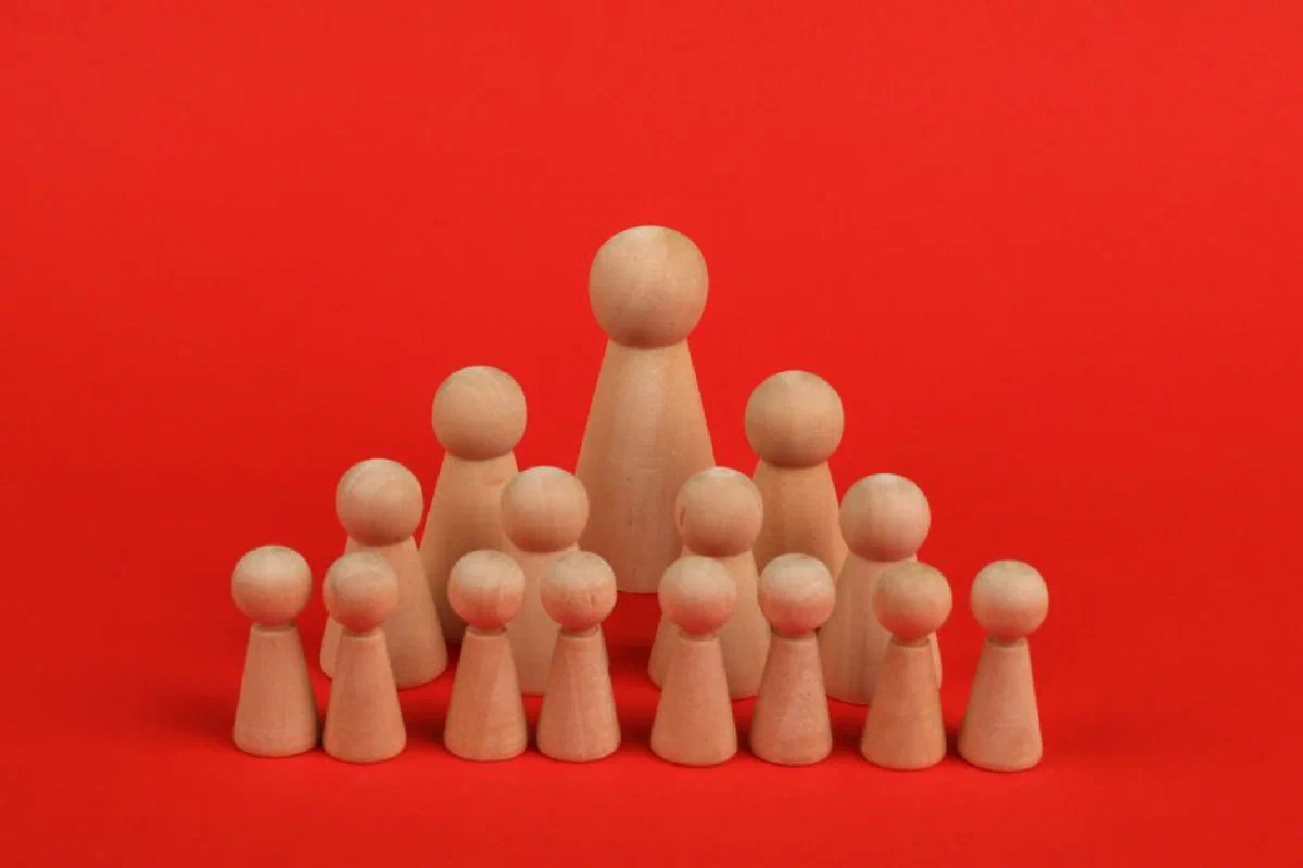 Wooden figurines arranged in hierarchy against bright red backdrop symbolizing leadership.
