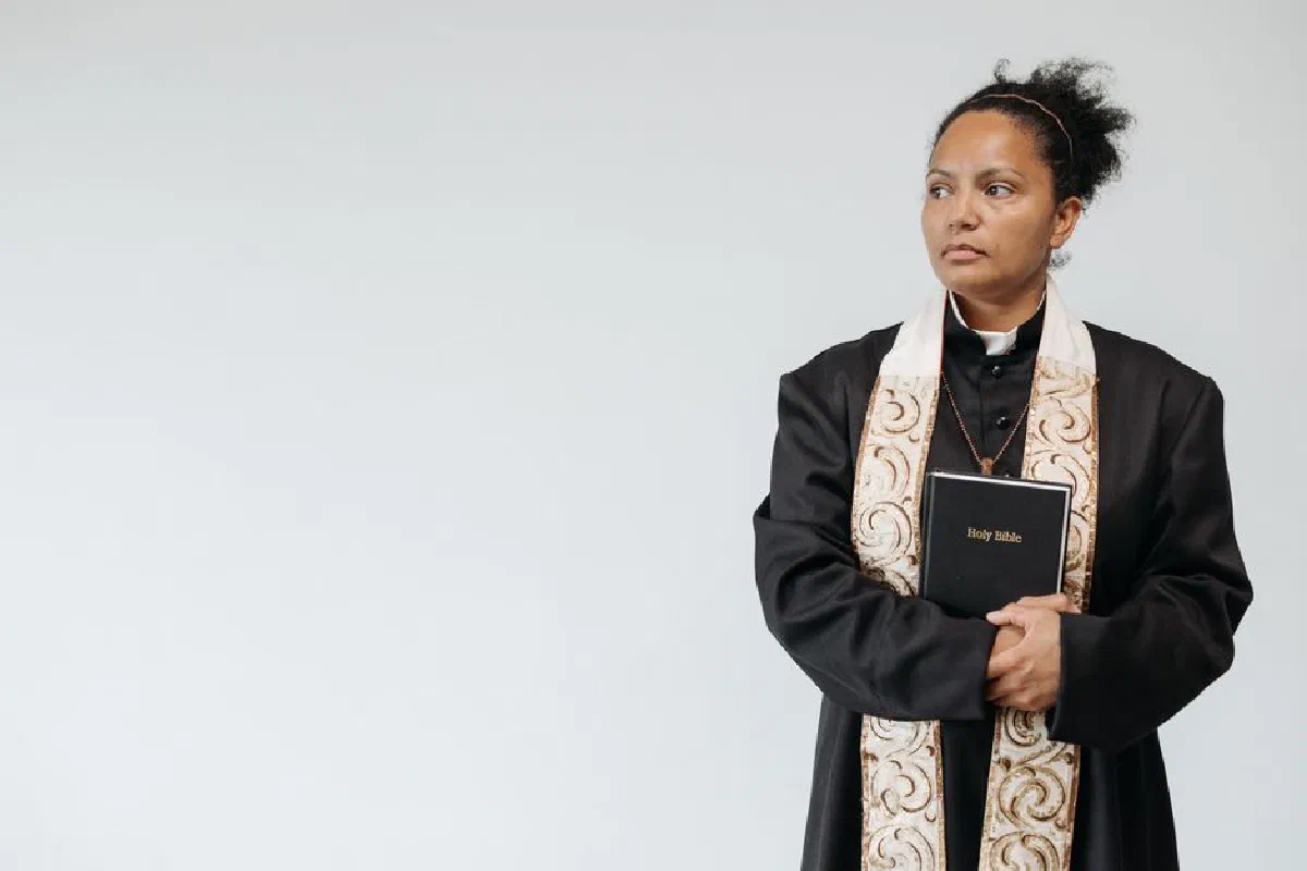 A female priest in religious attire holding a Holy Bible, symbolizing faith and spirituality.