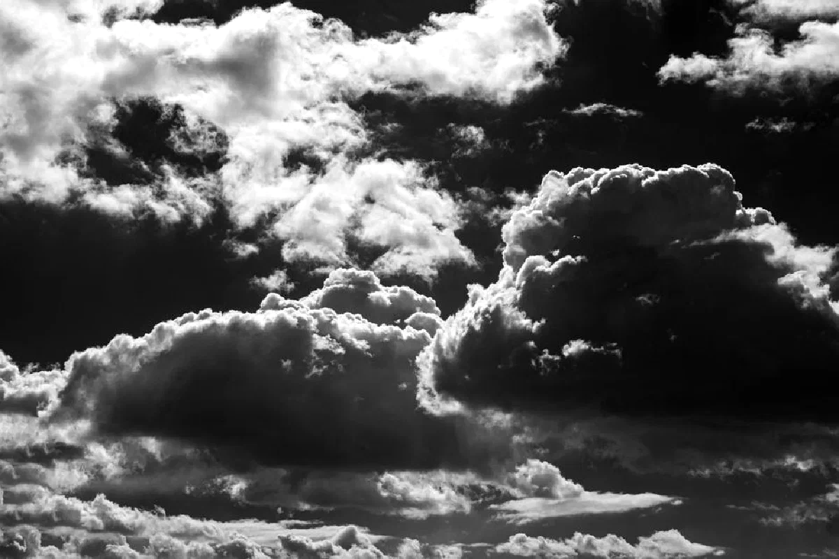 Moody and dramatic black and white photograph of dense, towering clouds in the sky.