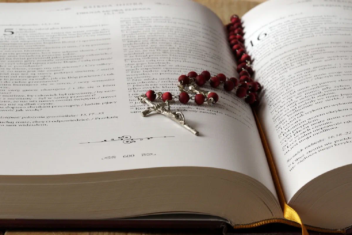 Open Bible with red rosary beads draped on pages, symbolizing faith and devotion.
