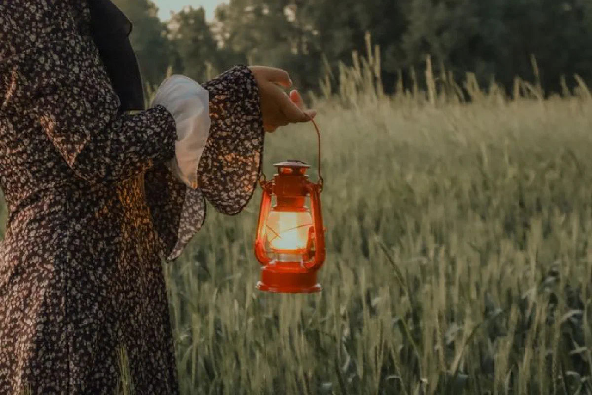 A serene scene with a woman holding a lantern in a grassy field during dusk, exuding a warm glow.