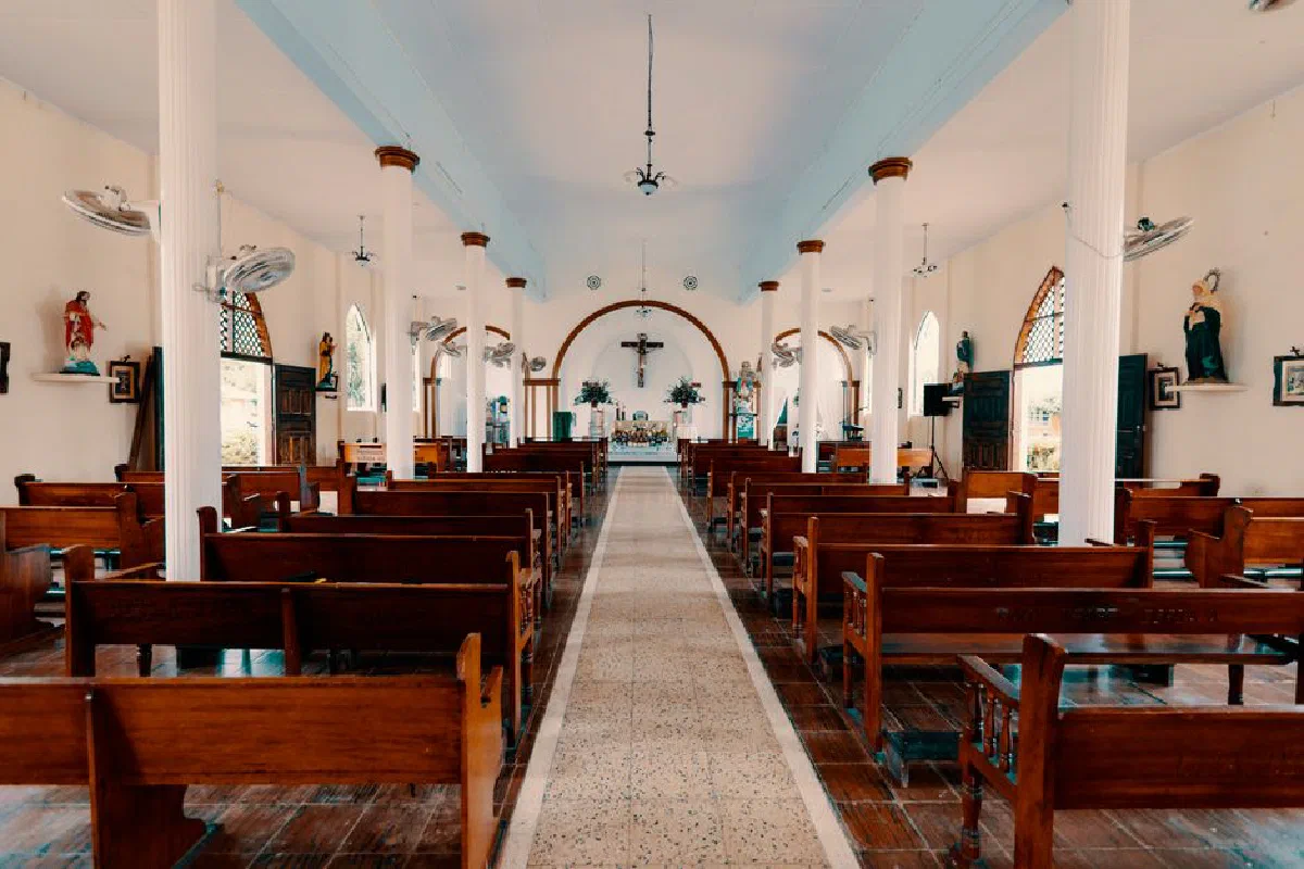 A serene view of the empty interior of a Catholic church, showcasing wooden benches and religious statues.