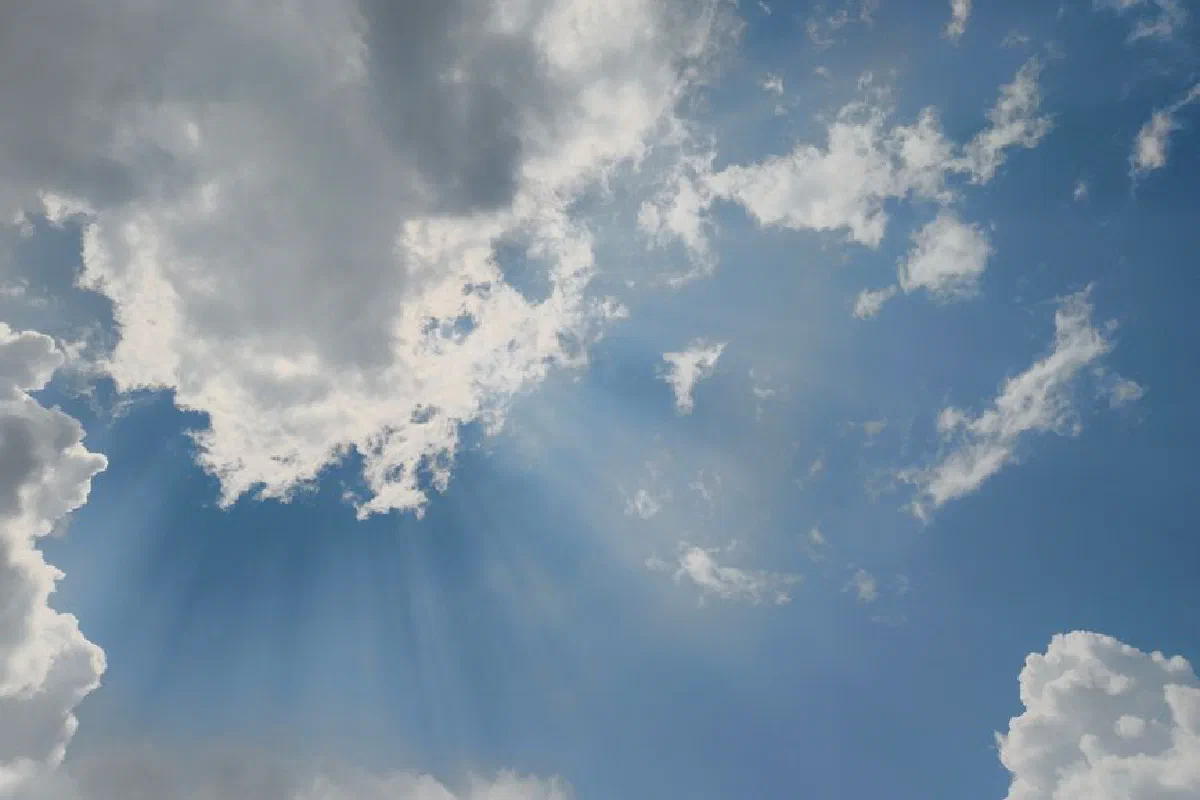 Captivating view of sun rays piercing through fluffy clouds in a bright blue sky.