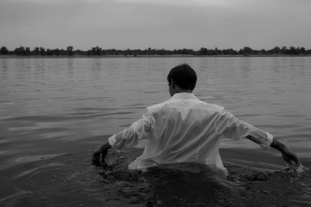 Black and white photo of a man walking into a lake, creating a serene and contemplative mood.