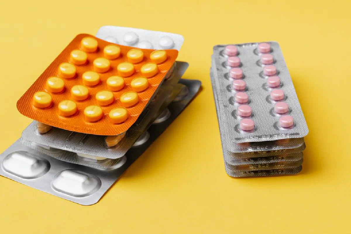 Heaps of various medication pills of different color and shape in blister packs placed on bright yellow background