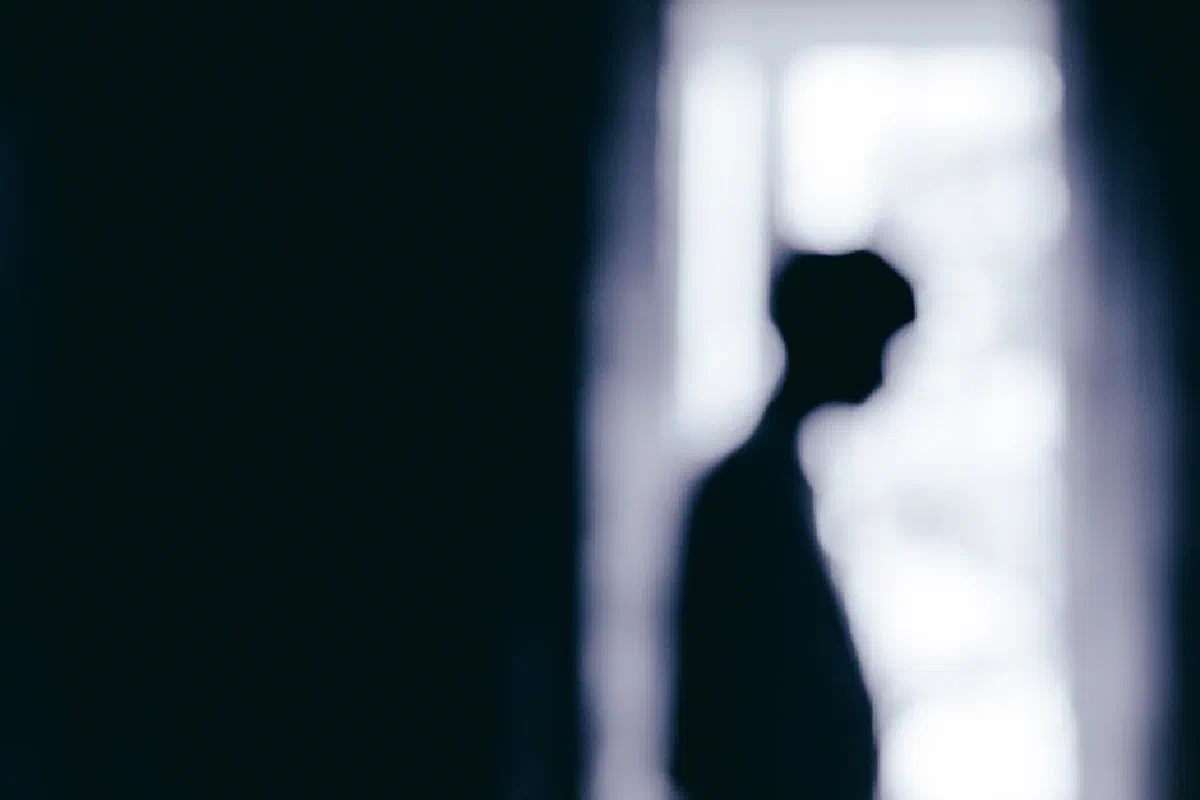 Blurred silhouette of a person standing near a window, creating a moody atmosphere.