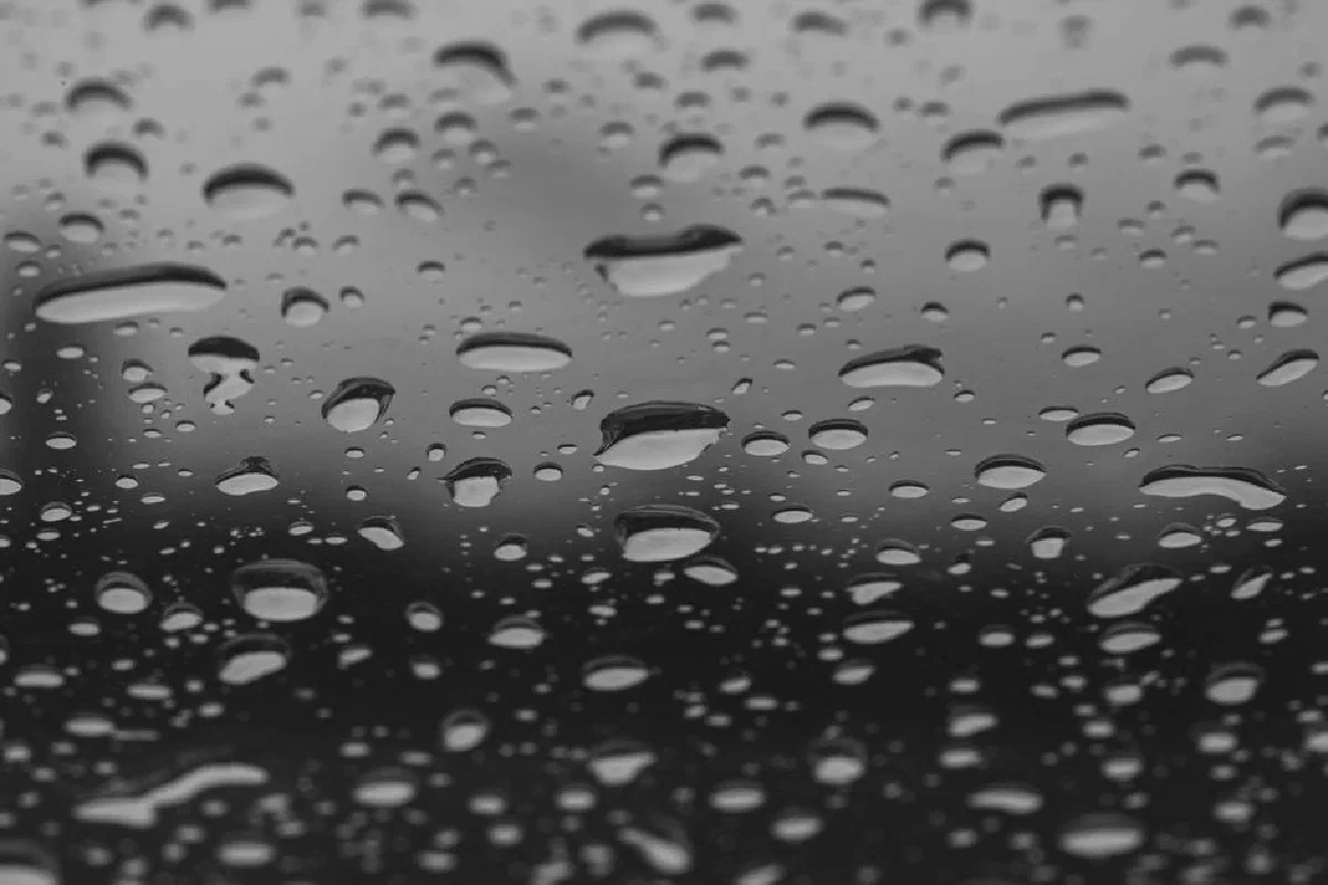 Black and white image of raindrops on a window creating an abstract and moody atmosphere.