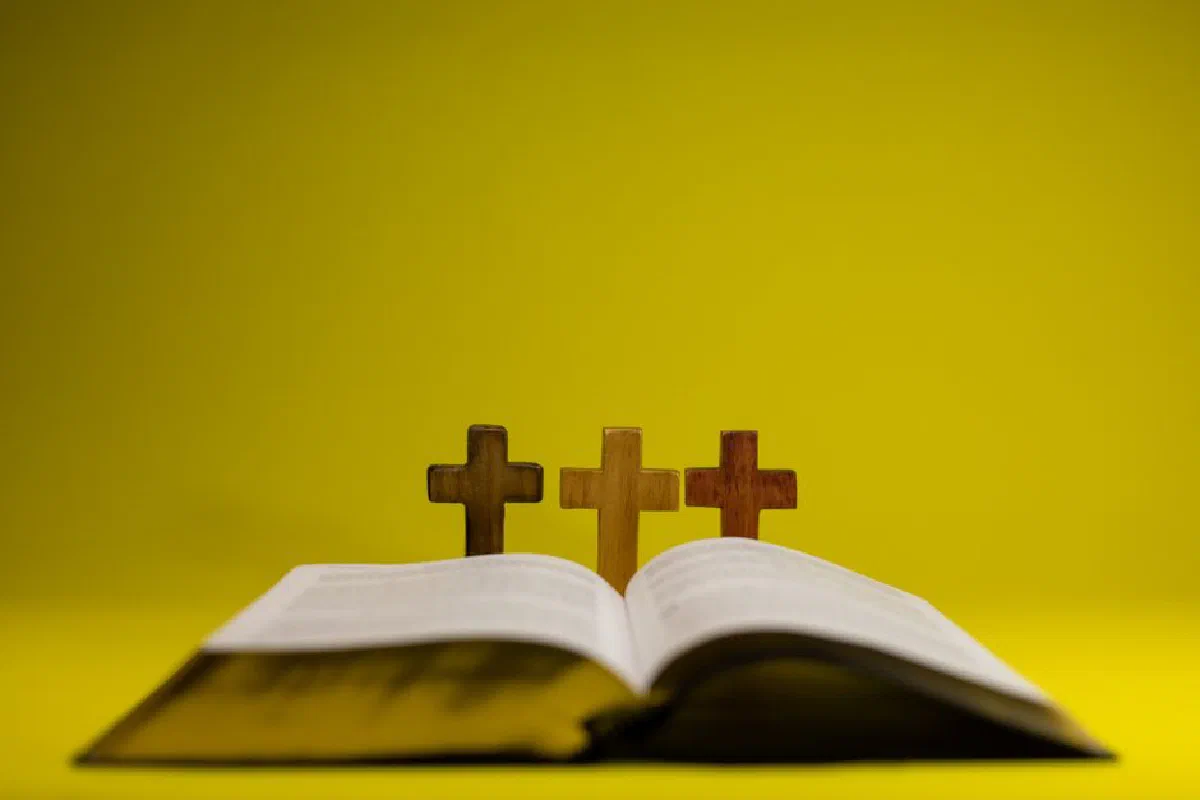 Open Bible with three wooden crosses symbolizing Christianity on a bright yellow background.