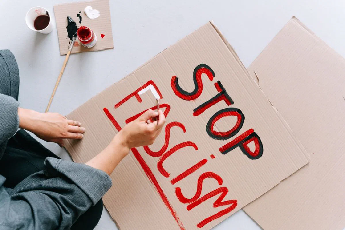 Person creating protest sign with "Stop Fascism" message, using red and black paint.