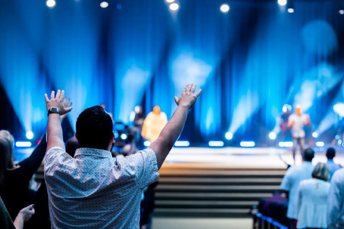 Group of people attending a lively worship service in a modern auditorium setting.