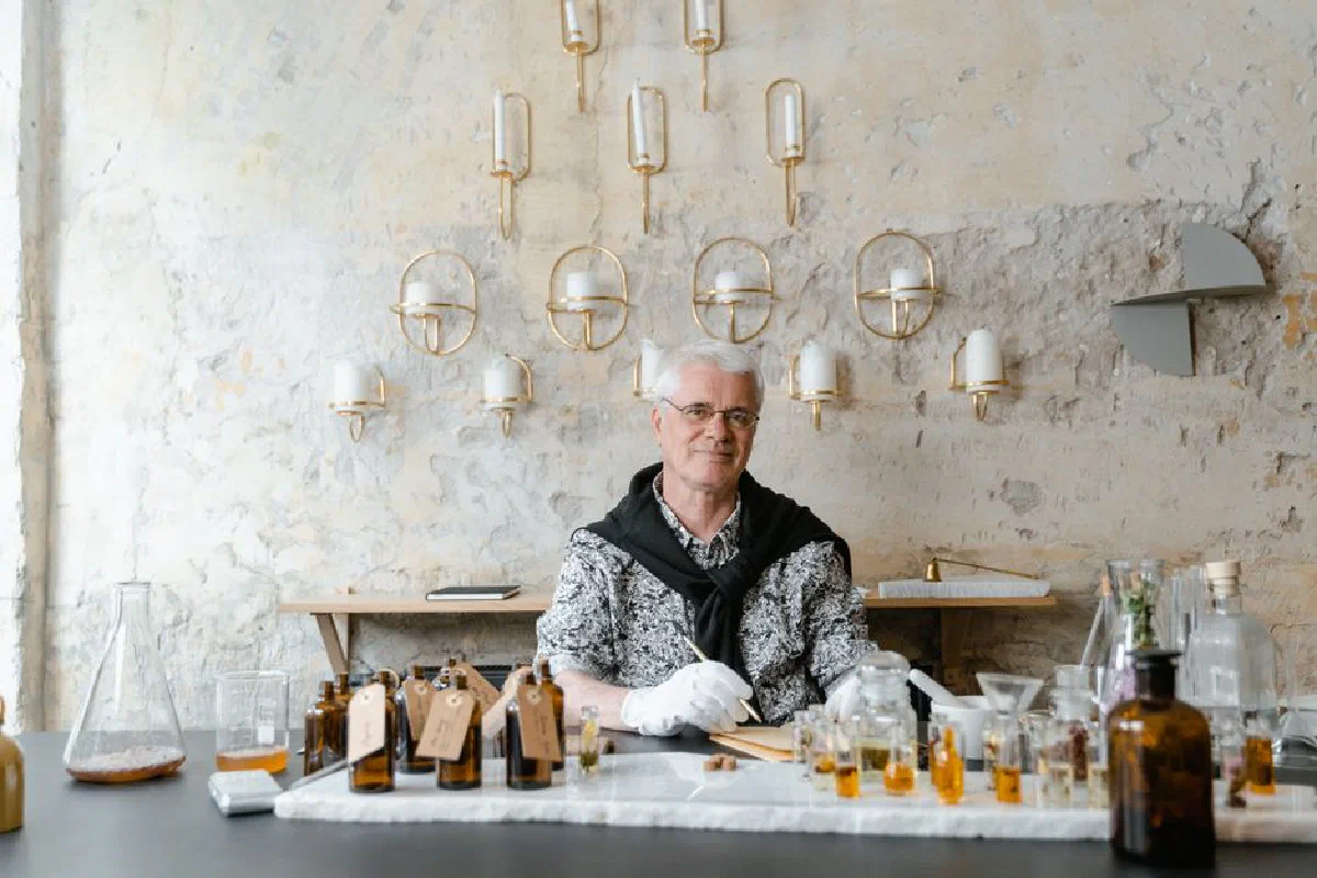 Senior male perfumer sitting among fragrance bottles in a rustic setting, creating unique scents.