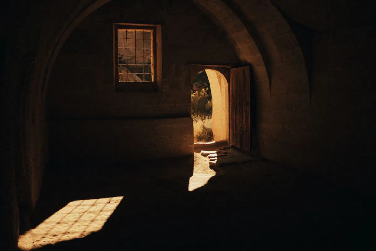 An ancient stone room with arched doorways and windows, casting dramatic shadows.