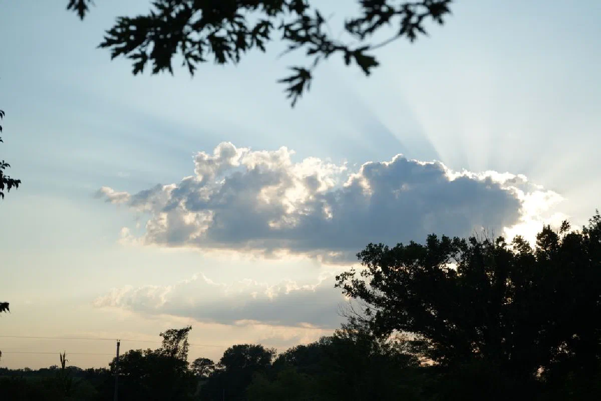Beautiful sunlight beams through fluffy clouds over a peaceful landscape of trees.