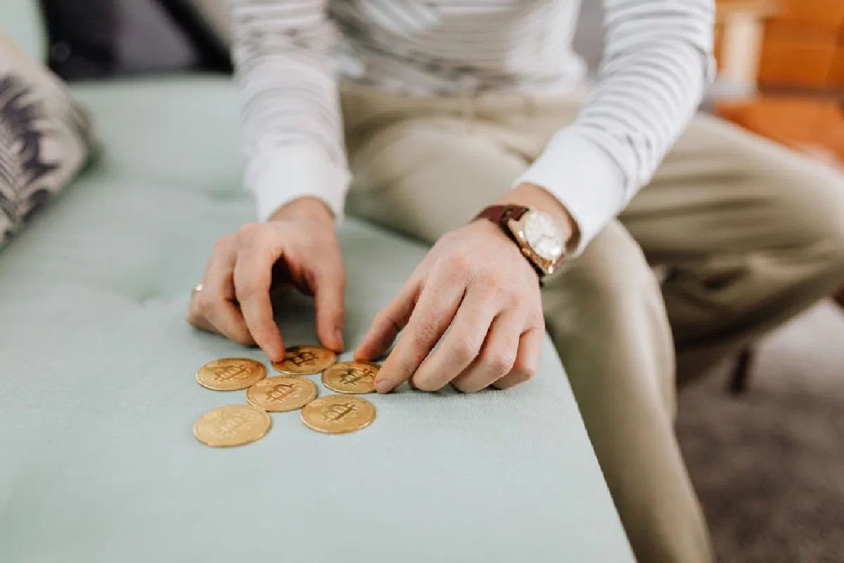 Close-up of hands organizing gold Bitcoin coins on a sofa, symbolizing digital currency management.