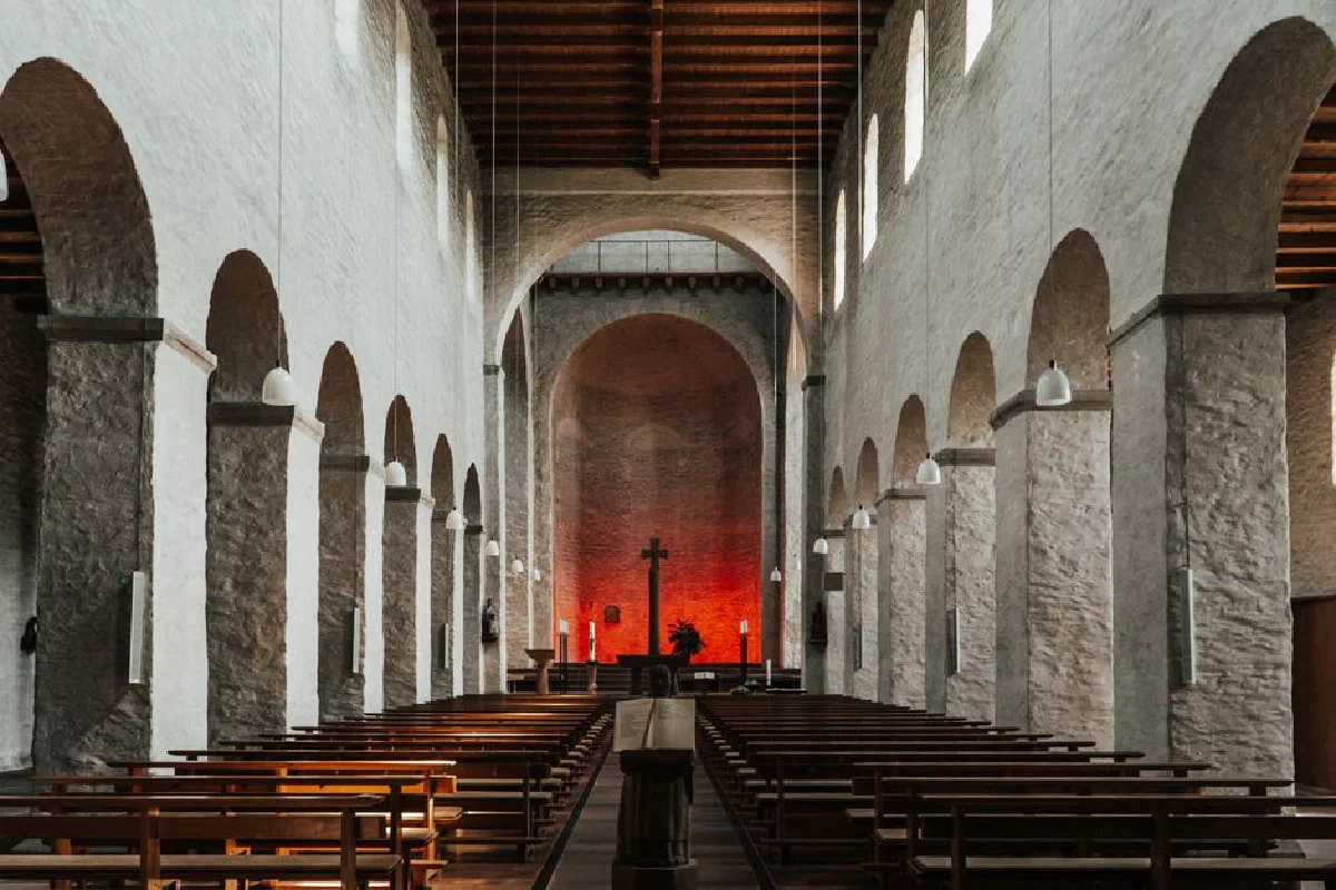 Elegant medieval church interior with arches, pews, and cross, illuminated by warm lighting.