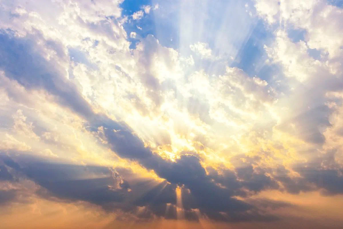 Vibrant sunrays piercing through scattered clouds during a sunset sky.