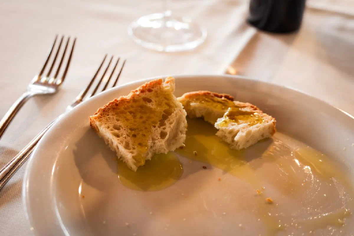 Close-up of bread with olive oil on a white plate at a restaurant table setting.