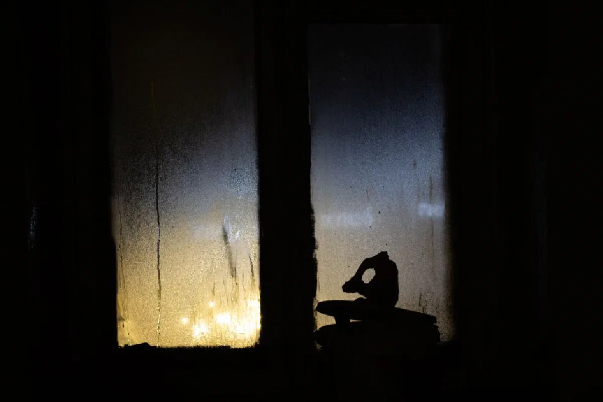 A moody silhouette in front of a wet, foggy window with lights at night, creating a contemplative atmosphere.
