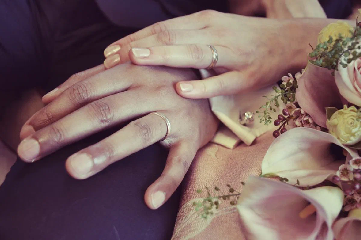 A close-up of a couple's hands wearing wedding rings, symbolizing love and commitment, surrounded by flowers.