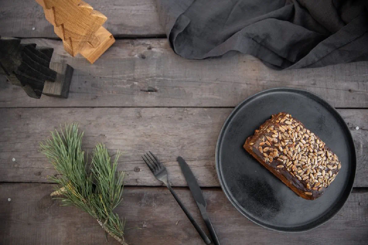 Freshly baked seeded bread loaf on a rustic wooden table with pine leaves.