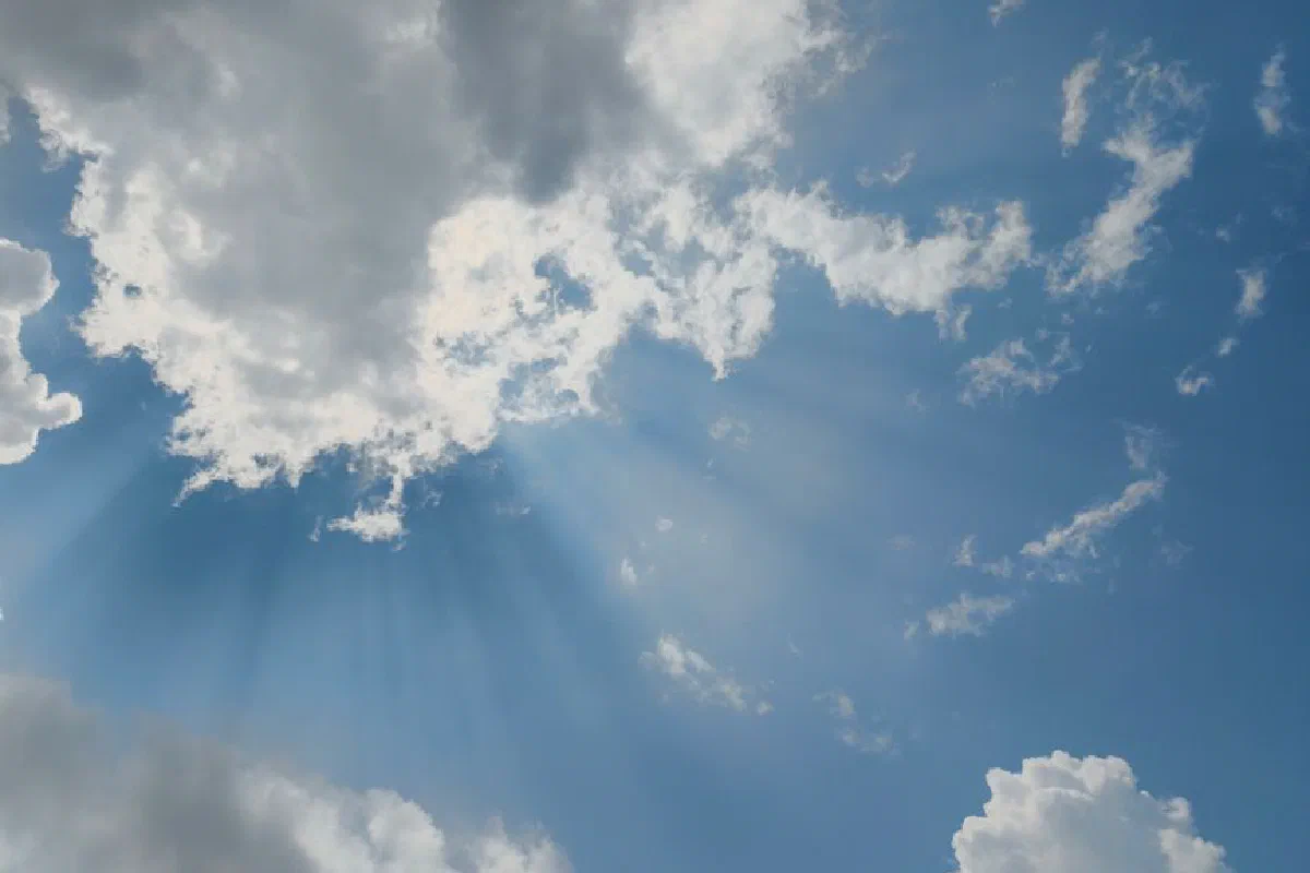 Beautiful sun rays streaming through fluffy clouds in a clear blue sky, captured in Silchar, India.