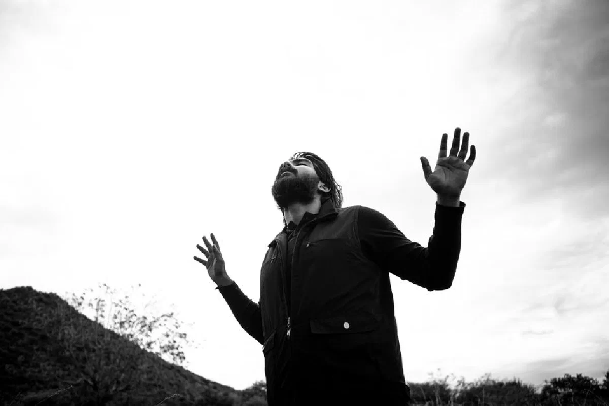 Grayscale image of a bearded man raising his arms outdoors, conveying freedom and expression.