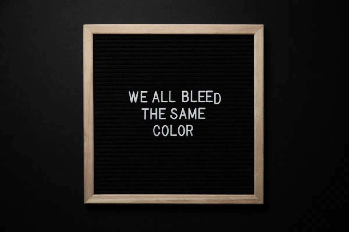 Top view of black signboard with phrase We All Bleed Same Color on surface on black background