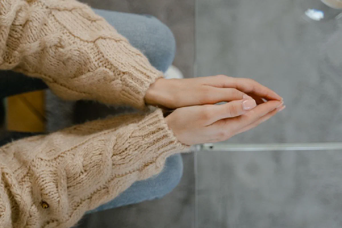 A close-up of clasped hands in a knitted sweater, viewed from above, conveying warmth and tranquility.