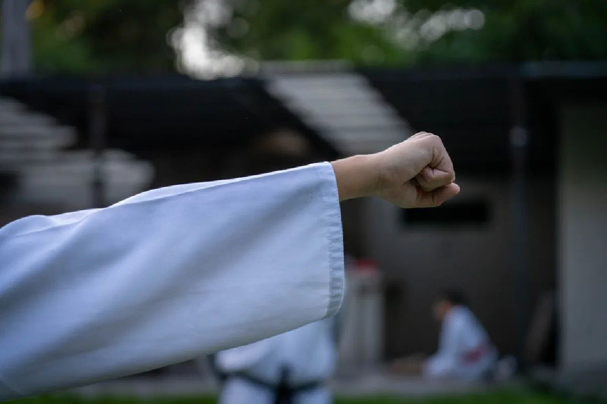 Close-up of a martial artist's fist in white uniform outdoors, symbolizing strength and focus.