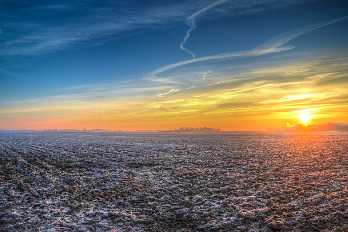 Vibrant sunrise over a frost-covered field with dramatic skies.