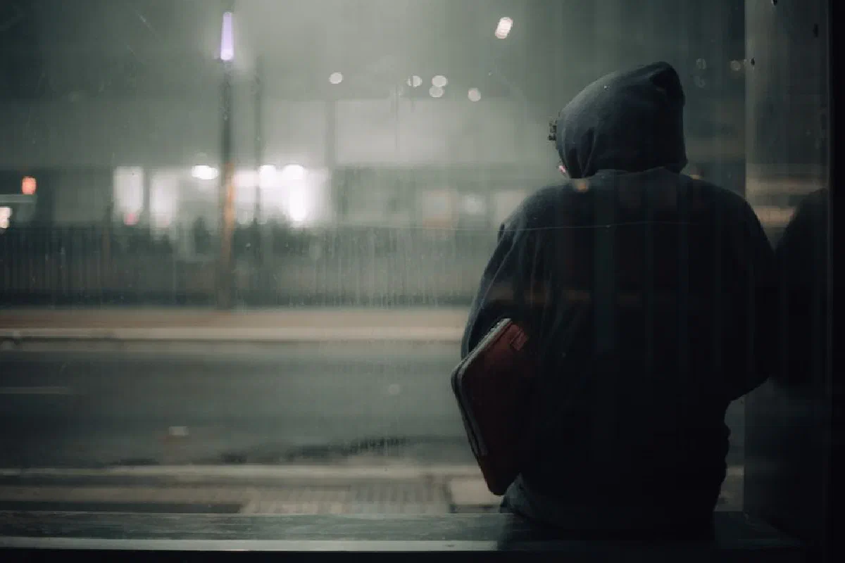 A person in a hoodie sits alone at night, reflecting in an urban setting.