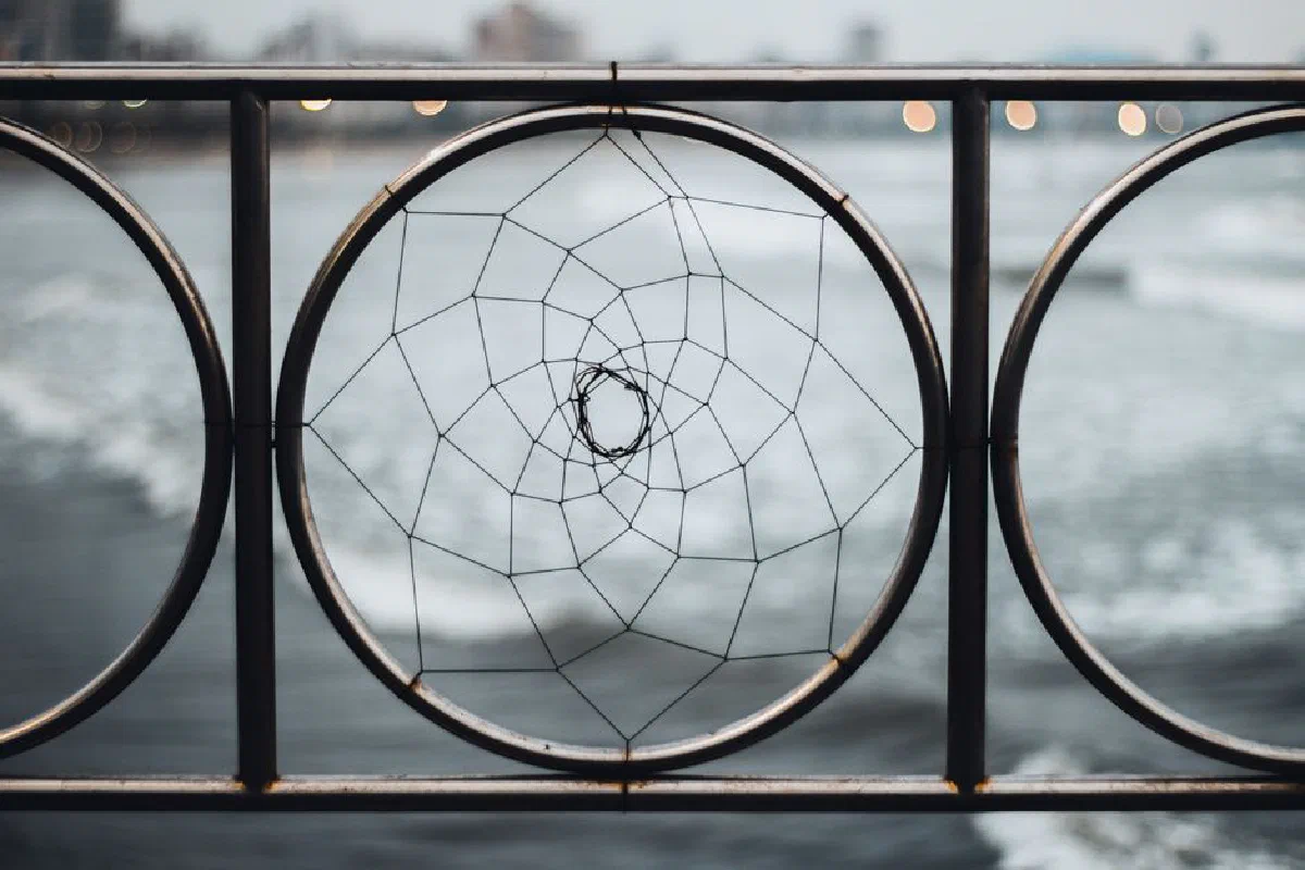 Close-up of a metal fence with a geometric design framing ocean waves, creating an artistic visual contrast.