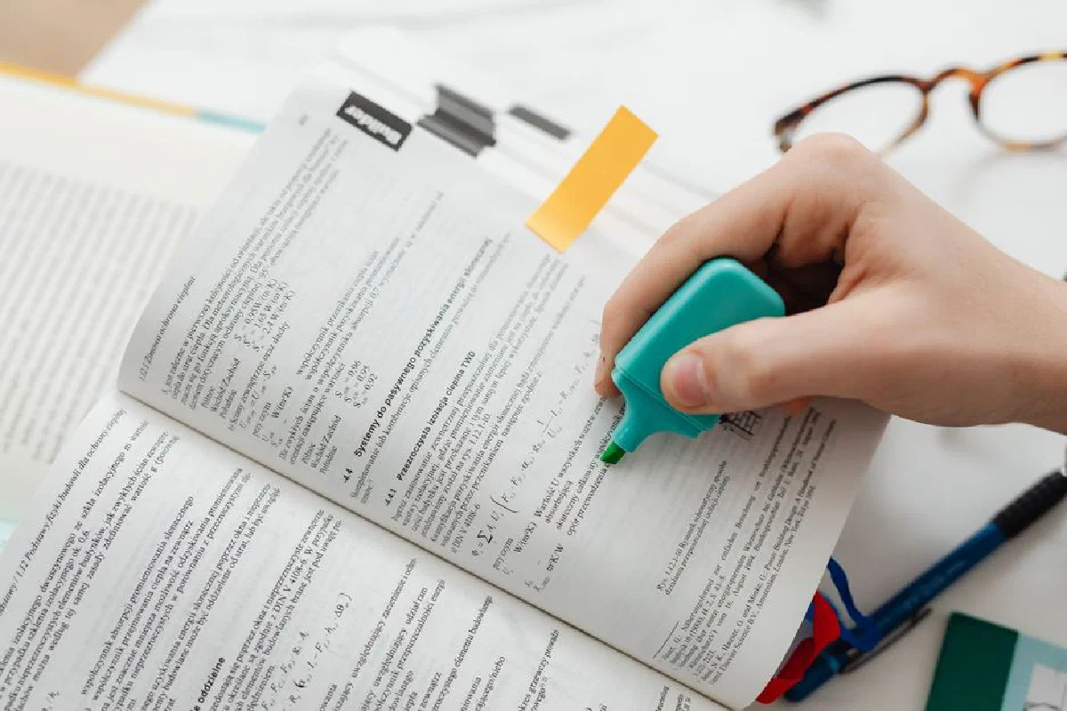 Close-up of a hand using a highlighter on an open textbook, focusing on key information.