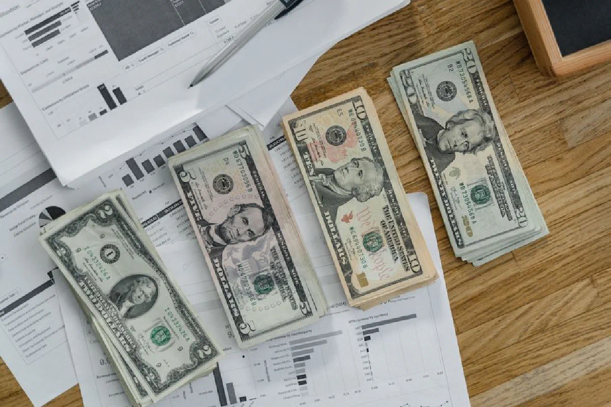 Stacks of US Dollar banknotes placed over financial documents and reports on a desk.