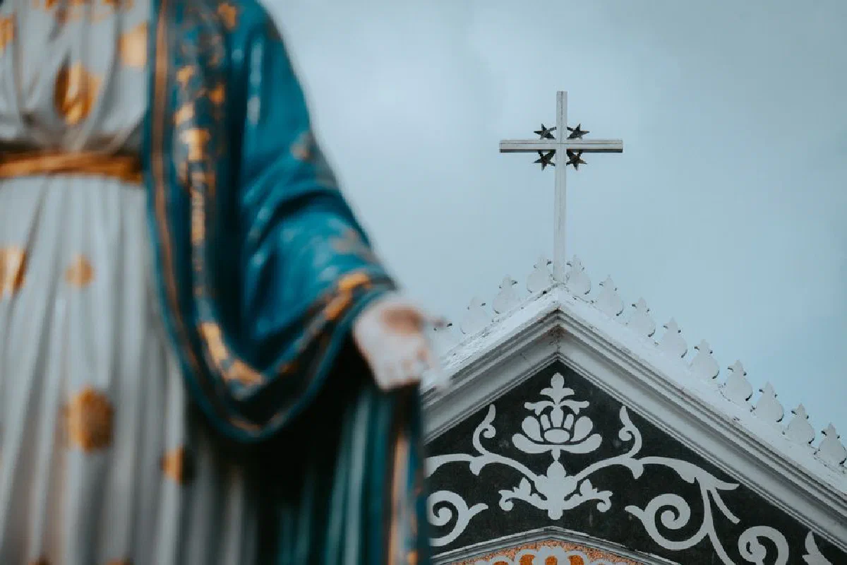 Close-up of a church facade featuring a cross and Virgin Mary statue in Gothic style.