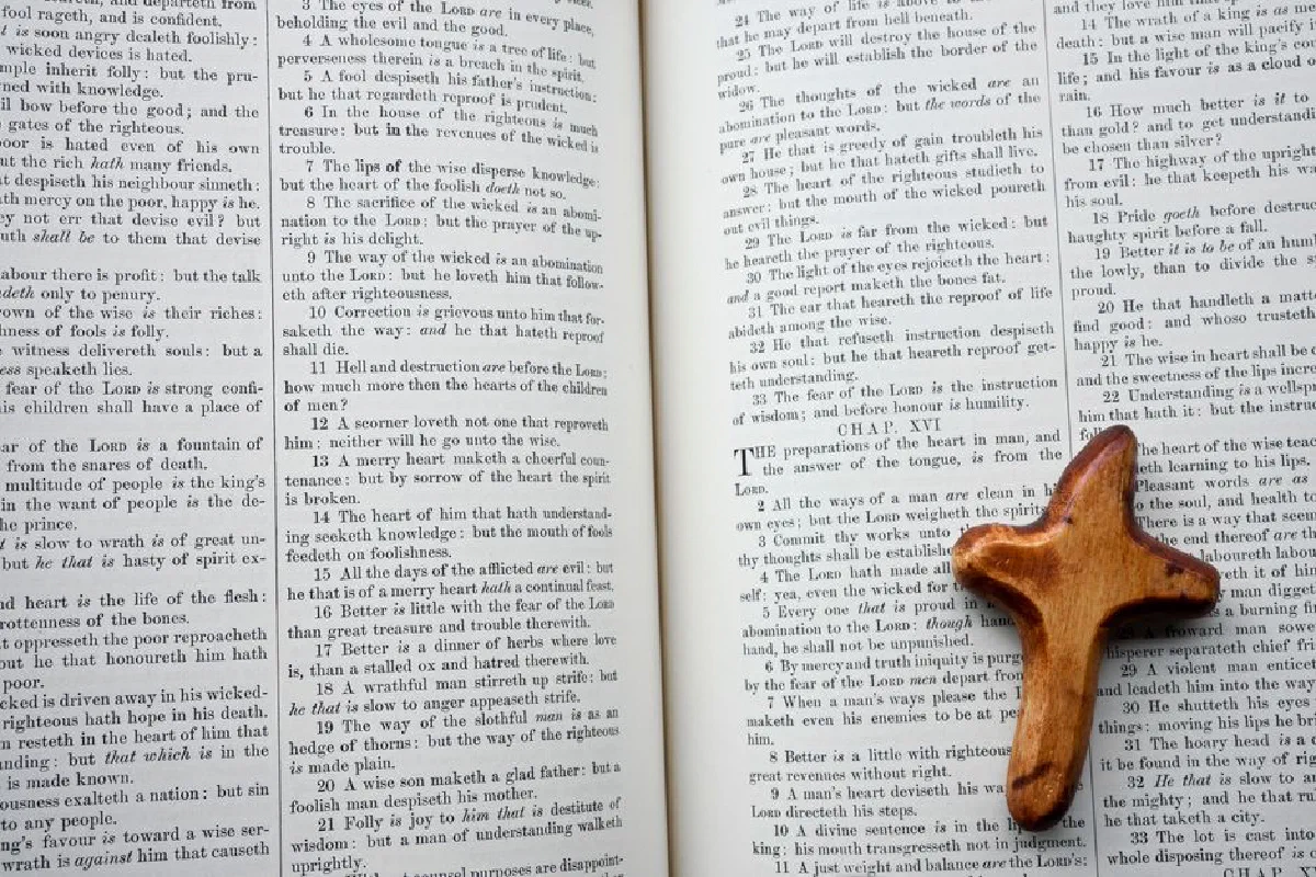 Wooden cross rests on an open Bible, highlighting scripture about wisdom and righteousness.