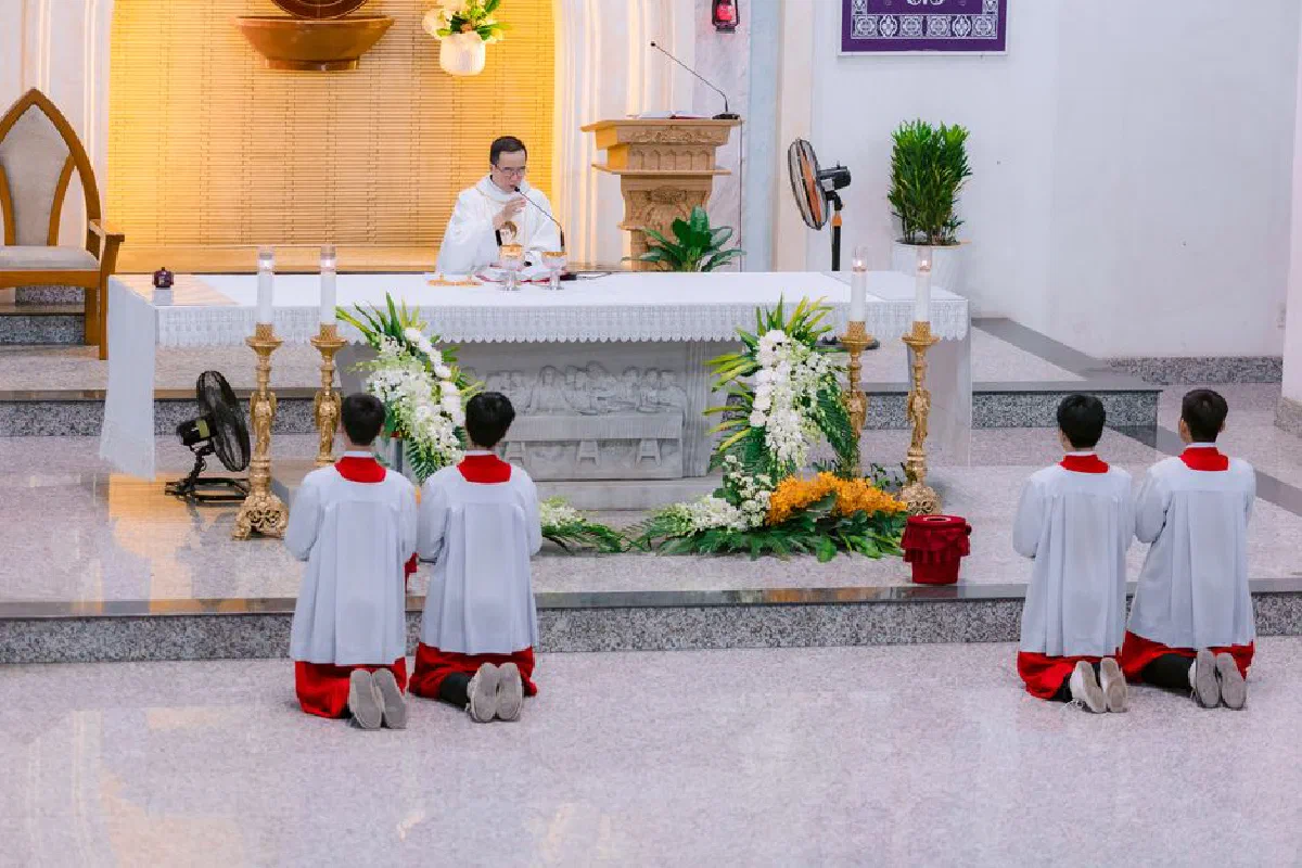 A priest conducts a mass ceremony with altar boys kneeling in a church.