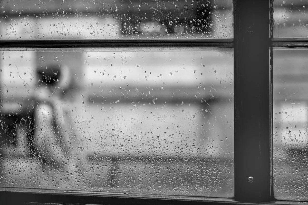 Raindrops on window with blurred city tram scene in Milan, Italy.